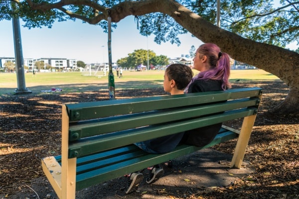 Mother and son sitting on a bench near a park